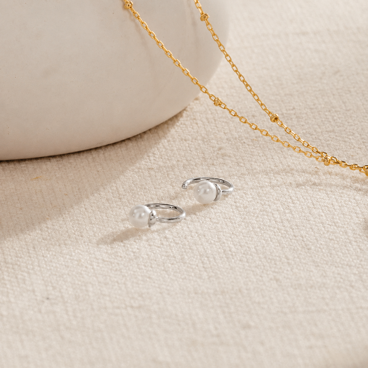 Silver earrings with a gold chain on a beige fabric background